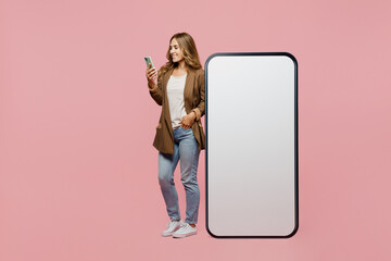 Full body young employee business woman she wear classic jacket near big huge blank screen mobile cell phone with workspace mockup area use smartphone isolated on plain pastel light pink background.