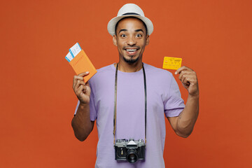 Traveler black man in purple t-shirt hat hold passport credit card isolated on plain orange color background Tourist travel abroad on weekends spare time rest getaway Air flight trip journey concept