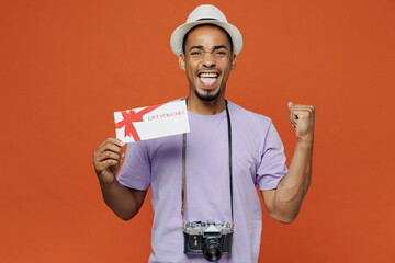 Traveler black man wear purple t-shirt hat hold coupon voucher do winner gesture isolated on plain...