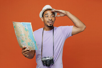 Traveler black man wear purple t-shirt hat hold read map look aside isolated on plain orange color background Tourist travel abroad on weekends spare time rest getaway Air flight trip journey concept