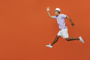 Fototapeta na wymiar Full body side view traveler black man wear purple t-shirt hat jump high run isolated on plain orange color background Tourist travel abroad in spare time rest getaway Air flight trip journey concept
