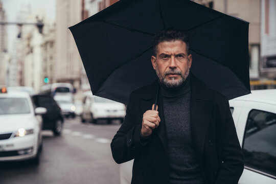 Thoughtful middle aged businessman with umbrella in street
