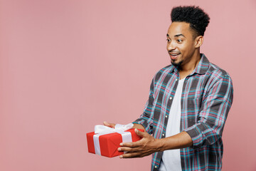 Young amazed happy man of African American ethnicity 20s he wear blue shirt hold red present box with gift ribbon bow isolated on plain pastel light pink background studio. People lifestyle concept.