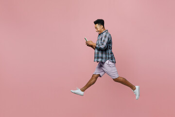 Fototapeta na wymiar Full body side view young man of African American ethnicity he wear blue shirt use mobile cell phone run fast jump high isolated on plain pastel light pink background studio. People lifestyle concept.