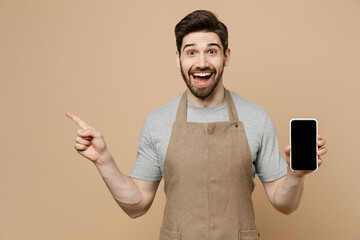 Young man barista barman employee wear brown apron work in coffee shop use mobile cell phone blank...