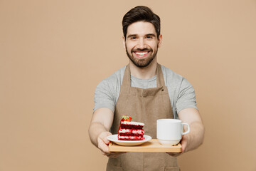 Young smiling man barista barman employee in brown apron work in coffee shop hold give cake tea sweet dessert breakfast isolated on plain pastel light beige background Small business startup concept