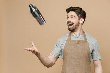 Young excited happy man barista barman employee in brown apron work in bar pub club toss up shaker...