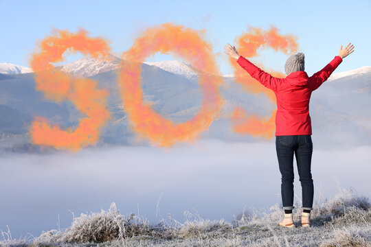 Woman and word SOS made of color smoke bomb in mountains, back view