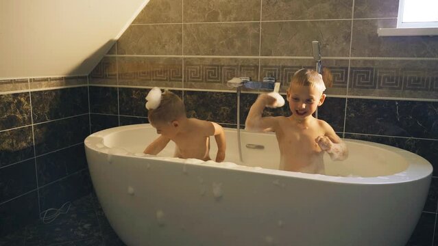 Joyful children in the bath play with foam. Children's games