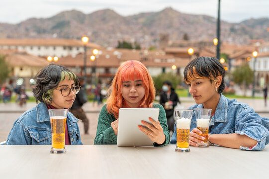 Young woman scrolling tablet while drinking beer with friends