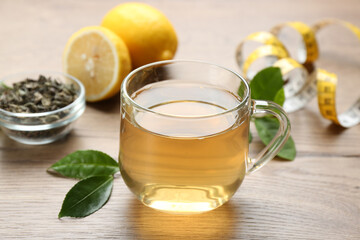 Herbal diet tea, lemon and measuring tape on wooden table