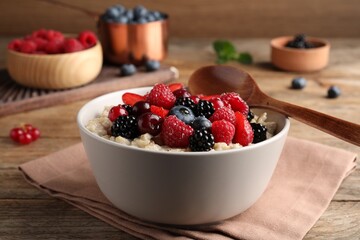 Bowl with tasty oatmeal porridge and berries served on wooden table. Healthy meal