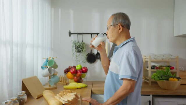 Asian senior mature male drinking a glass of milk in kitchen at home.