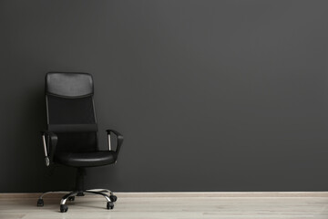 Comfortable office chair near black wall indoors. Space for text