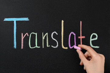 Woman writing word Translate with chalk on blackboard, closeup