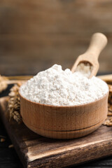 Fototapeta na wymiar Wheat flour in bowl, spike and grains on black table, closeup