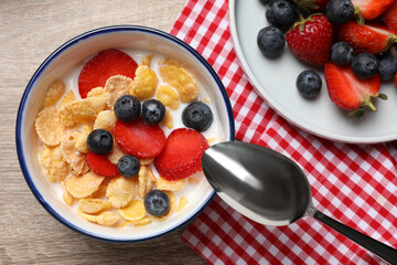 Delicious crispy cornflakes with milk and fresh berries on wooden table, flat lay