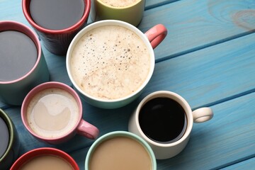 Many cups of different coffee drinks on light blue wooden table, above view