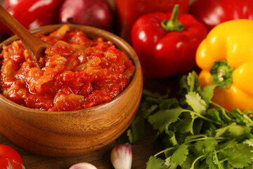 Tasty lecho in wooden bowl and fresh ingredients on table, closeup