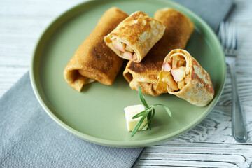 Pancakes stuffed with apples on a green plate with a cube of butter and a sprig of rosemary.