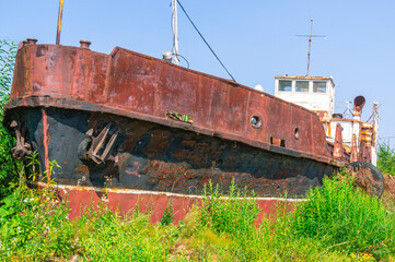 Old rusty ships lie on the sandy shore. Abandoned ships against a background of green bushes and...