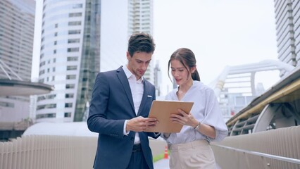 Caucasian businessman and Asian woman worker walk outdoors in the city