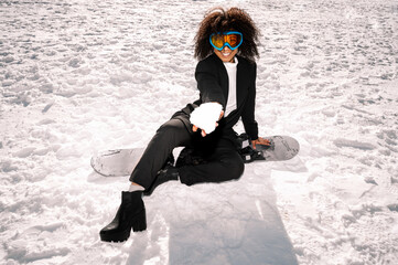 African American woman with goggles and a snowboard on a snowy mountain during winter
