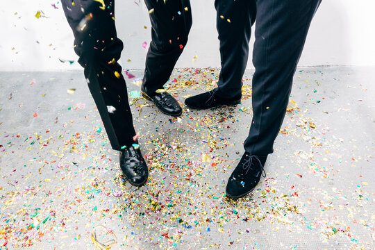 Crop stylish friends celebrating festive event with confetti on floor