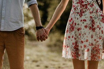 A couple in love is standing next to each other and holding hands. Man and woman are wearing summer dress and clothes. Outdoor date. Trendy fashionable clothing.