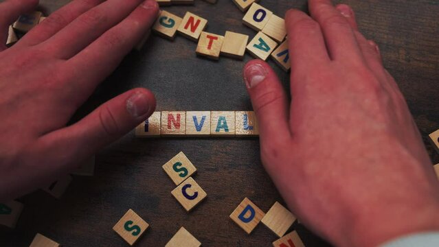 Symbolic concept represented by the wordplay INVALID. Numerous square wooden puzzles with colourful letters on them placed on a dark wooden table. . High quality 4k footage