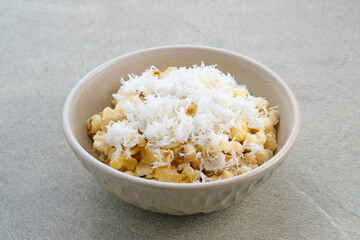 Grontol Jagung or Corn grontol is a traditional snack in Indonesia. Boiled shelled corn sprinkled with grated coconut. Served in a bowl on grey background.