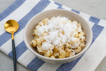 Grontol Jagung or Corn grontol is a traditional snack in Indonesia. Boiled shelled corn sprinkled with grated coconut. Served in a bowl on grey background.