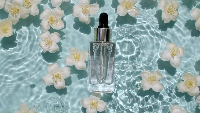 Cosmetic bottle, vial and jasmine petals flowers on water surface with drops. Pure water with reflections sunlight and shadows. Slow motion of waves water. Design, advertising, products. 4k
