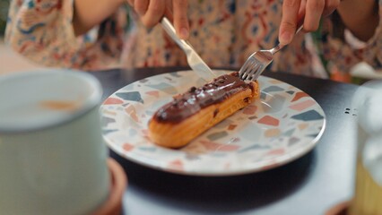 Fototapeta na wymiar Female hands cutting eclair on a plate with knight and fork