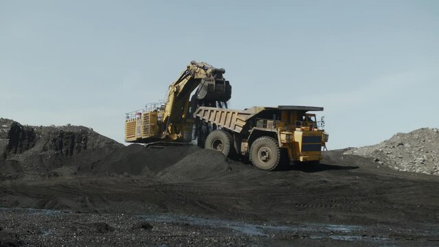 Excavator boom with bucket filled with coal turns and spills into back of truck