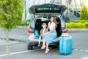 a mother with a child son in the car and a blue suitcase are going on vacation or a trip sitting in front of the airport