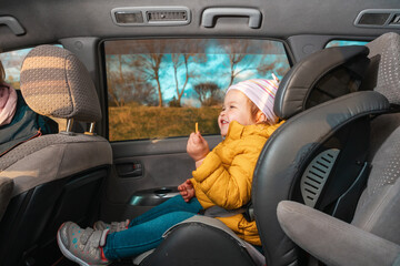 Happy little baby girl sitting in a child seat in the back seat of a car. The concept of safe automobile trip and child health insurance - obrazy, fototapety, plakaty