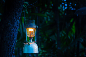 Vintage oil lamp hanging on a tree in the forest in the evening camping atmosphere.Travel Outdoor...