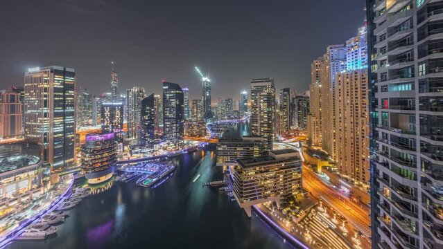 Aerial panoramic view to Dubai marina skyscrapers around canal with floating boats day to night transition timelapse. White boats are parked in yacht club after sunset