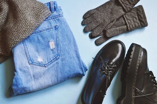 Gray wool scarf, blue jeans, boots and gloves flat lay photography. Fall and winter women's clothes, fashion outfit