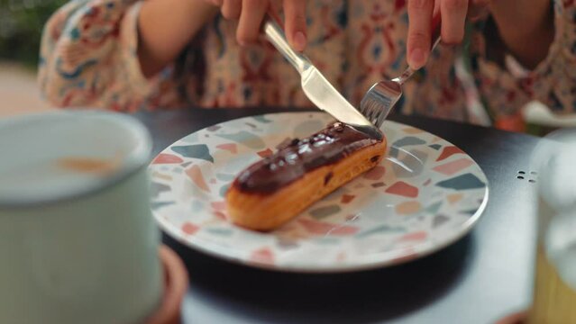 Female hands cutting eclair on a plate with knight and fork