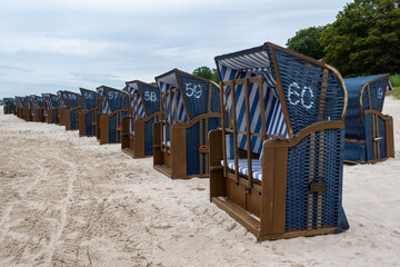Rows of blue beach rattan huts on a beach on a cloudy day. No tourists on the beach.