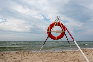 Fototapeta premium An orange lifeboat and reach extenders stuck in the sand on the beach. In the background, a view of the sea and clouds on the horizon
