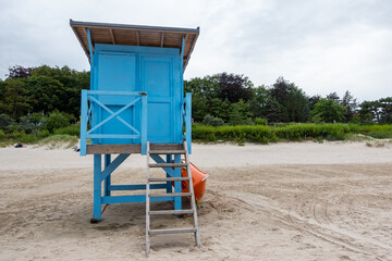 Fototapeta na wymiar A blue lifeguard booth on the beach on a cloudy day. Orange lifeboat leaning against the side of the house.