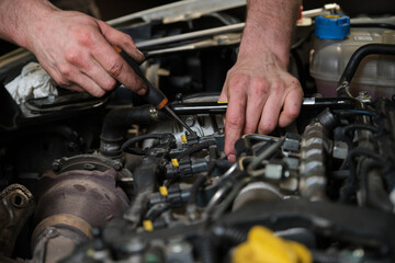 Close up of car mechanic hands removing fuel injectors in engine room checking dust and test pressure in maintenance process.