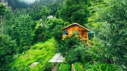 male tourist on balcony of beautiful wooden tiny treehouse in the mountains of Jibhi India on cloudy day