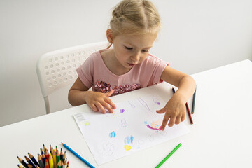 Blonde child girl draws with colored pencils sitting at the table