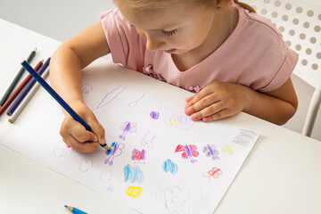 Child girl draws with colored pencils on white paper. Top view, flat lay