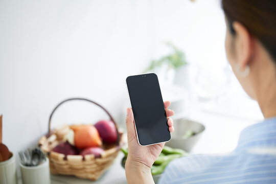 キッチンで料理を作りながらスマホを見る女性