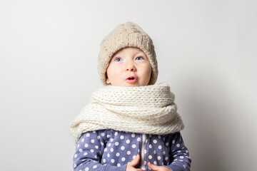 beautiful little baby in a hat is surprised on a light background. Concept of children's emotions, winter, shopping